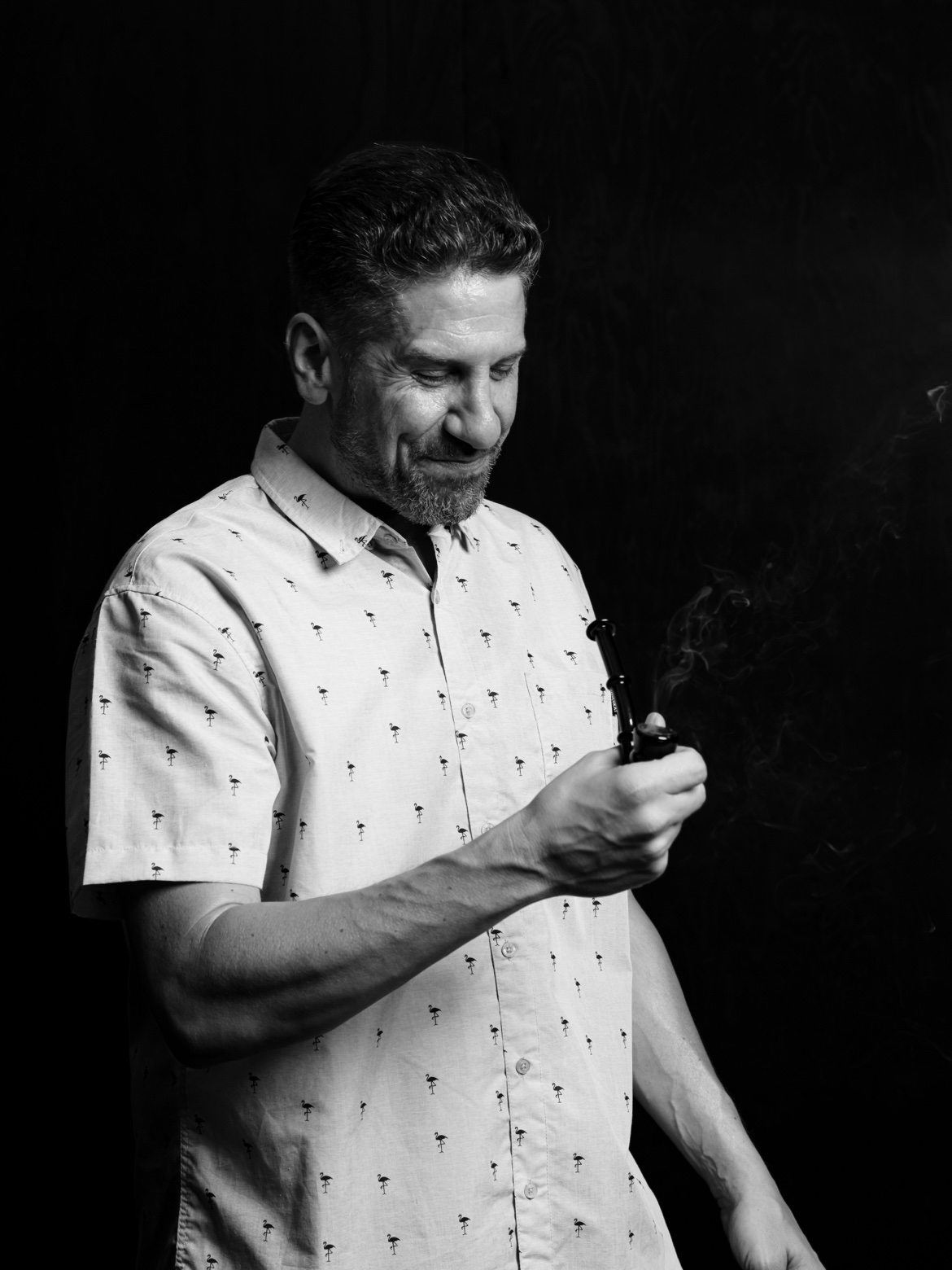 Black and white studio portrait of Brian Holler smiling with a pipe